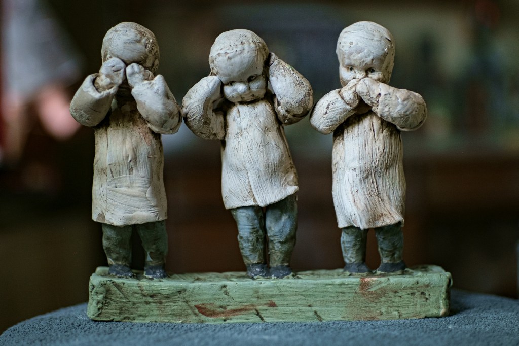 Sculpture of three children with their eyes and ears covered, standing on a green base.