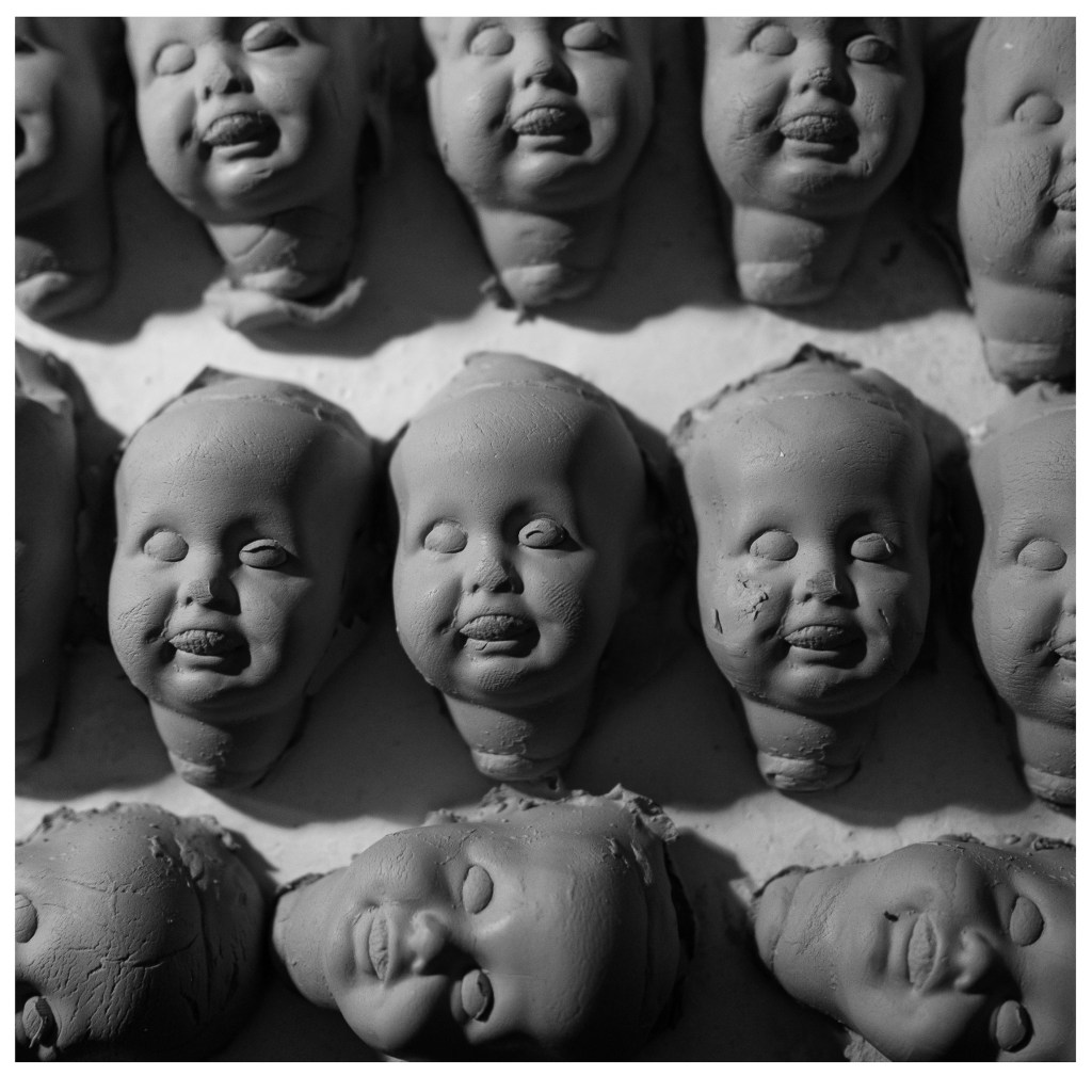 Clay doll heads arranged in a grid pattern, featuring neutral expressions and textured surfaces.