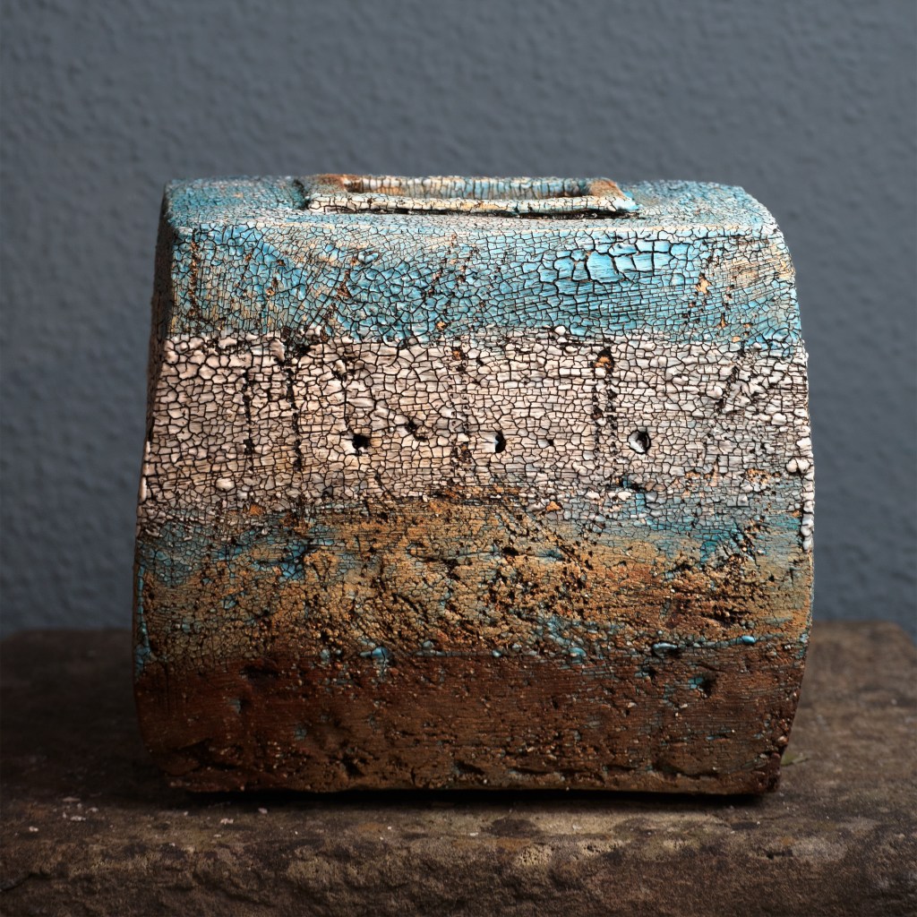 Keramisches Kunstwerk mit einer strukturierten, rissigen Oberfläche in Blau- und Erdtönen.